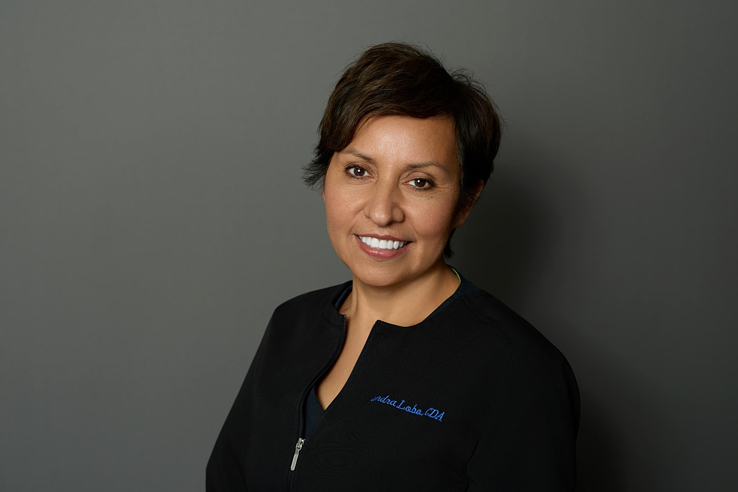 Smiling professional in dental attire, gray background.